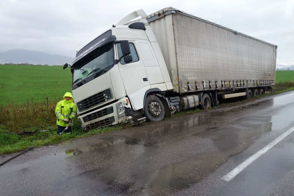 A truck rests in a ditch following a road accident on a rainy autumn day, while rescuers provide assistance at the scene.