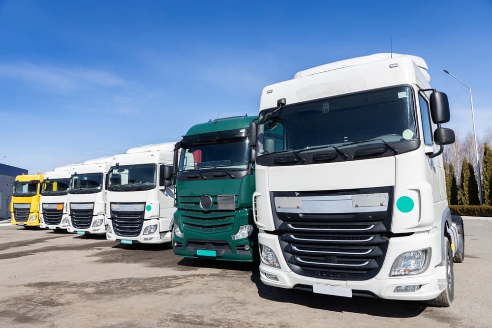 A row of tractor-trailers neatly parked in a lot on a sunny day, showcasing the vibrant cabs of trucks in various colors.