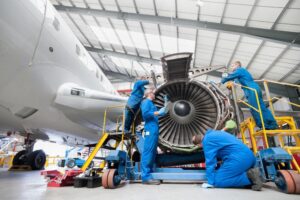 A team of engineers, dwarfed by the aircraft's scale, meticulously assemble a giant engine. Tools glint in their hands as they work with practiced efficiency, a symphony of clicks and whirrs filling the air.