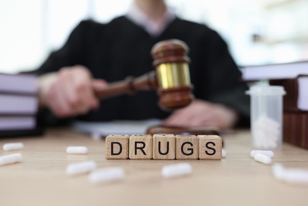 Word 'Drugs' Made of Cubes and Scattered Pills on Judge's Counter in Courtroom, Symbolizing Action Against Illegal Narcotics and Drug Dealers.